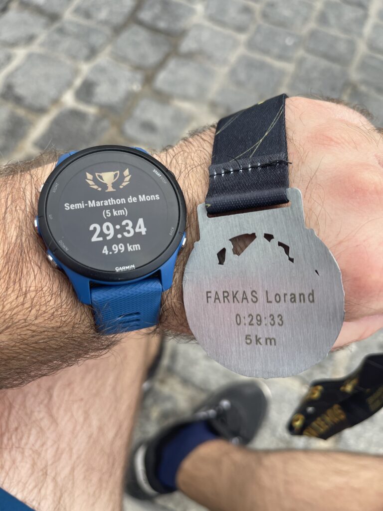 Selfie showing left arm with running watch and engraved medal after completing first official 5K.