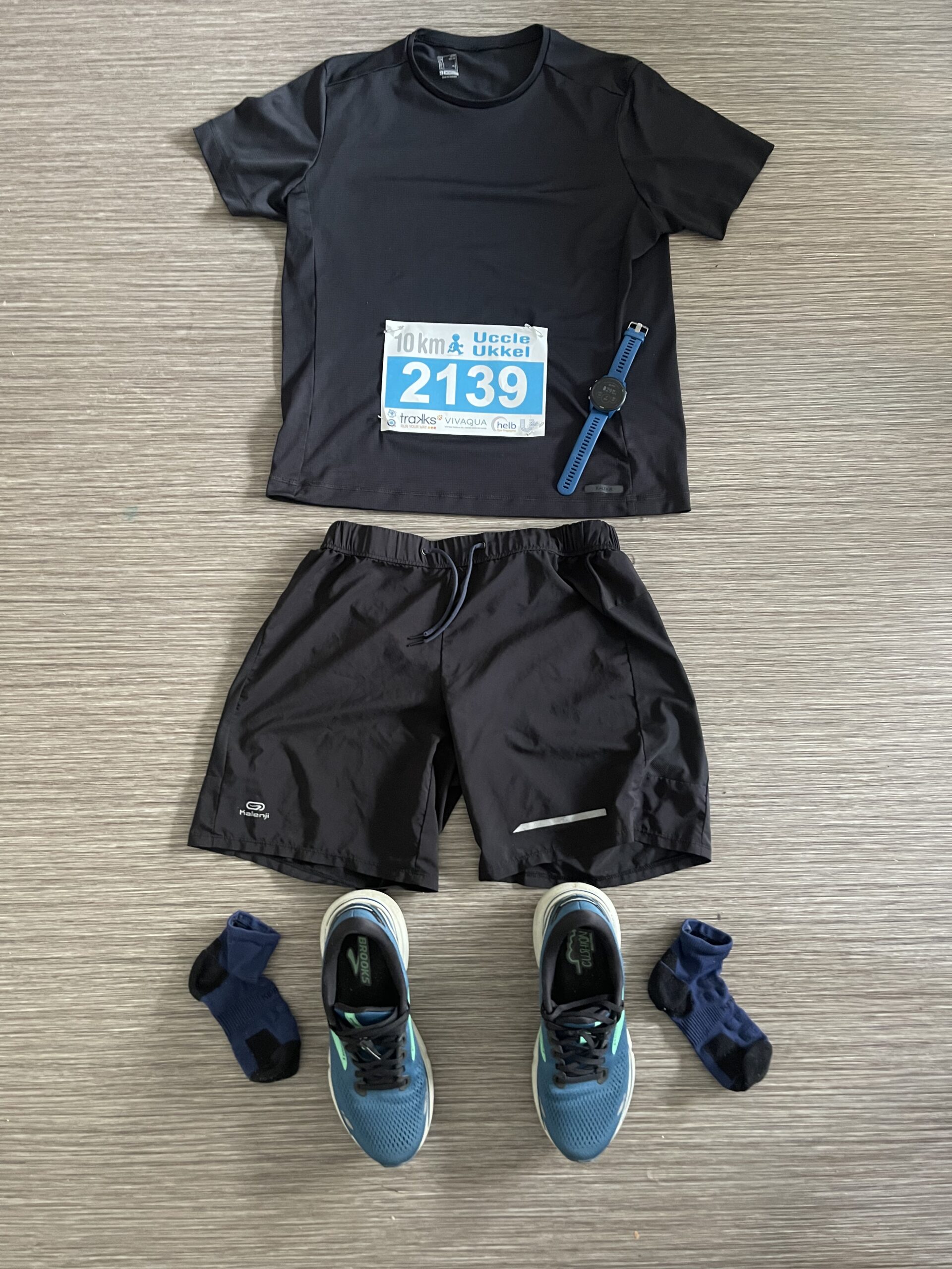 Flat lay of minimalist running gear for a first 10K race, featuring shirt, shorts, watch, socks, and shoes.