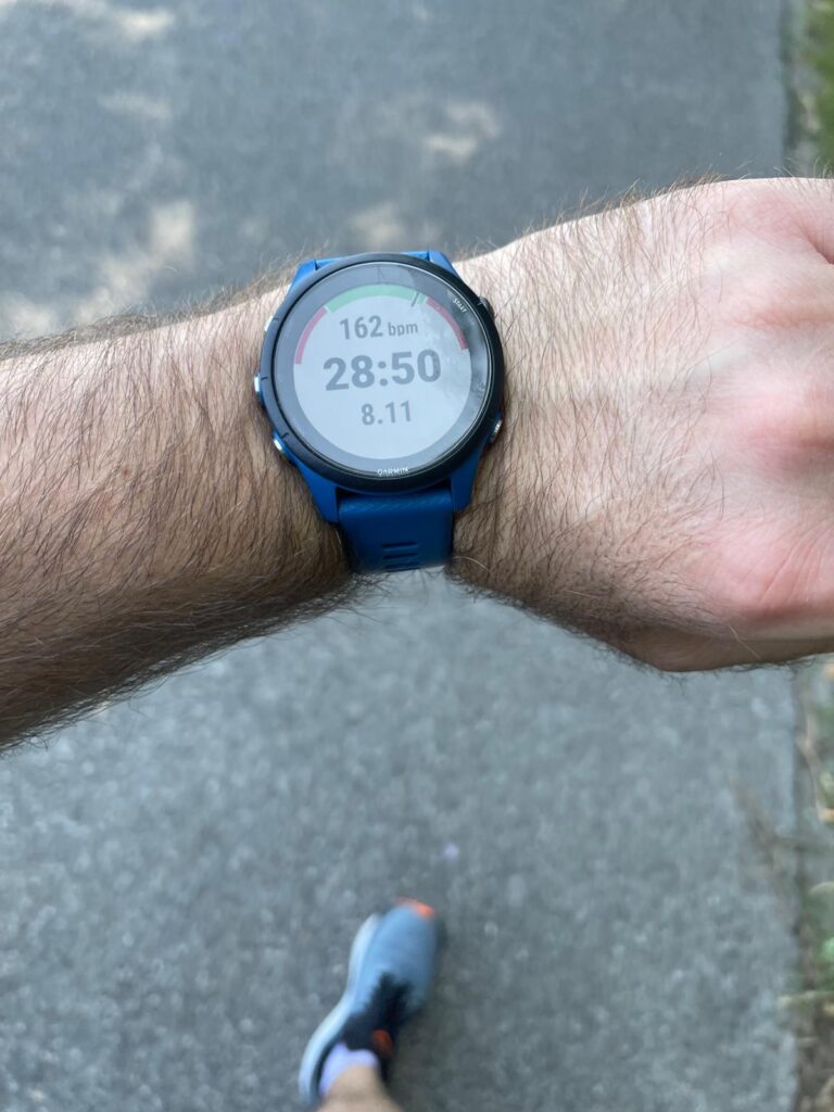 Close-up of a runner’s wrist wearing a Garmin Forerunner 255, showing heart rate, elapsed distance, and remaining time during a workout guided by Garmin’s adaptive training plan.