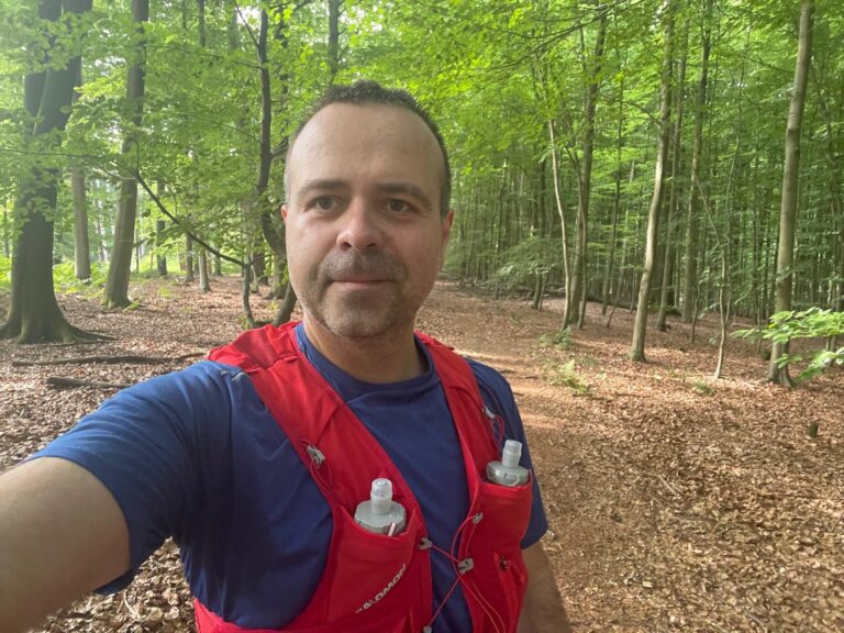 Loránd taking a selfie during a forest trail run, wearing the red Salomon ADV Skin 12 hydration vest.