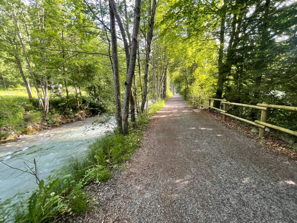 Sunny trail run in Chamonix with a river along the route, unpaved road, and wooden fence.