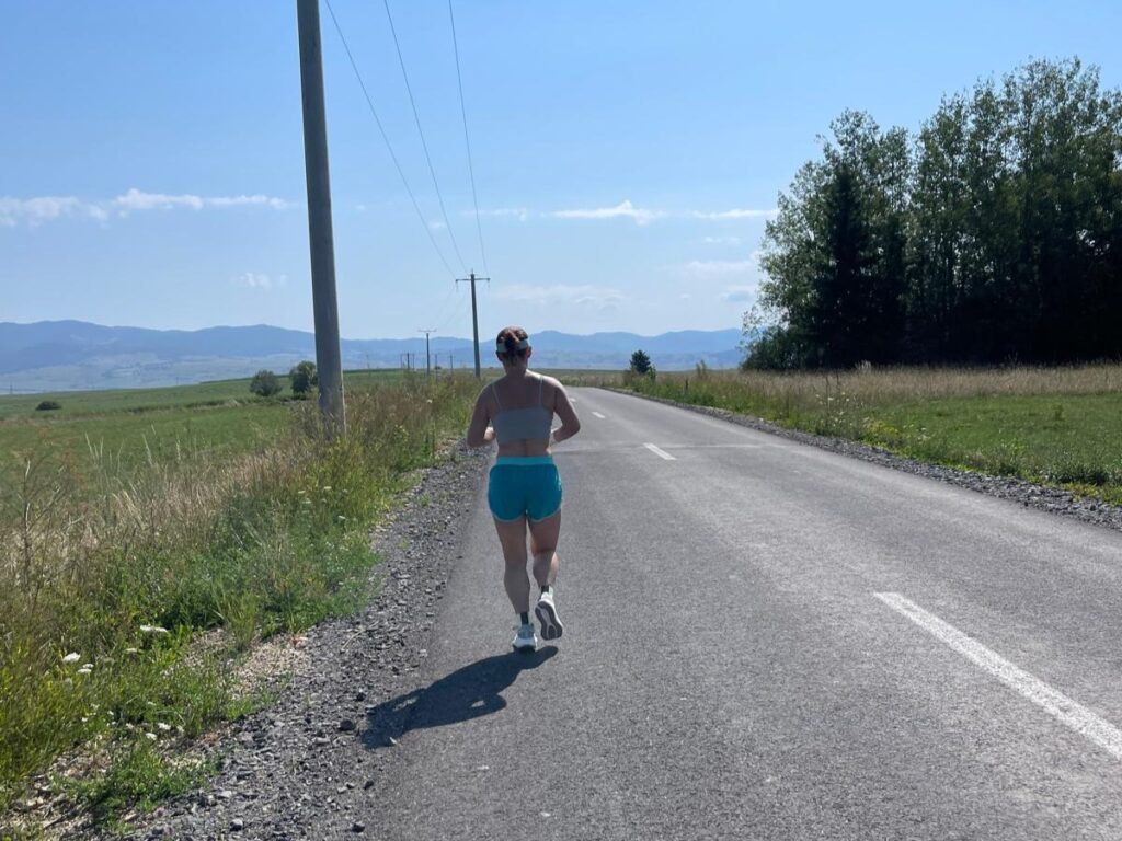 Woman running on a sunny day on a countryside road, surrounded by trees and fields, enjoying ideal running conditions.