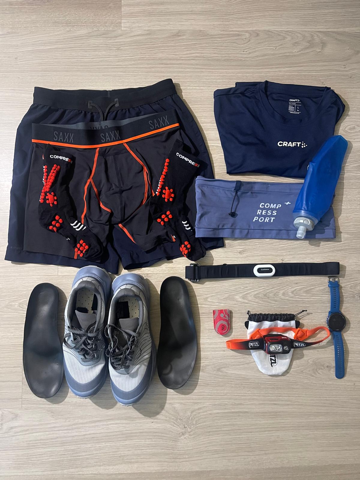 Flat lay photo of current running gear including shoes, insoles, compression socks, running belt, watch, and hydration flask.