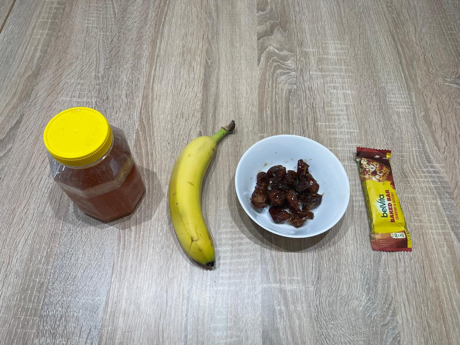 Natural running fuel including a banana, honey, cereal bar, and dates used for quick energy before or during a run.