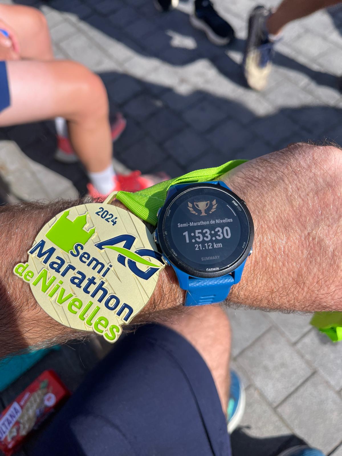 Runner sitting after finishing the 2024 Semi-Marathon de Nivelles, Garmin Forerunner 255 showing race stats, medal around wrist, celebrating sub-2-hour finish.