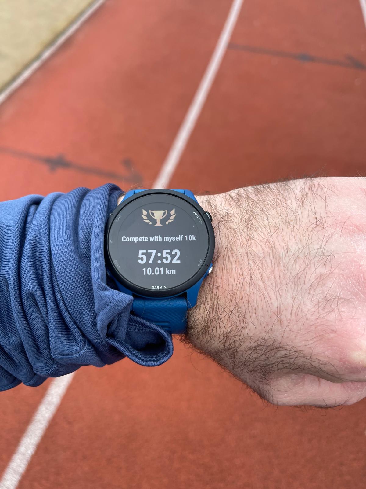 Garmin Forerunner 255 showing a 10 km custom event called “Compete With Myself” on a running track during a sub-1 hour 10K test.