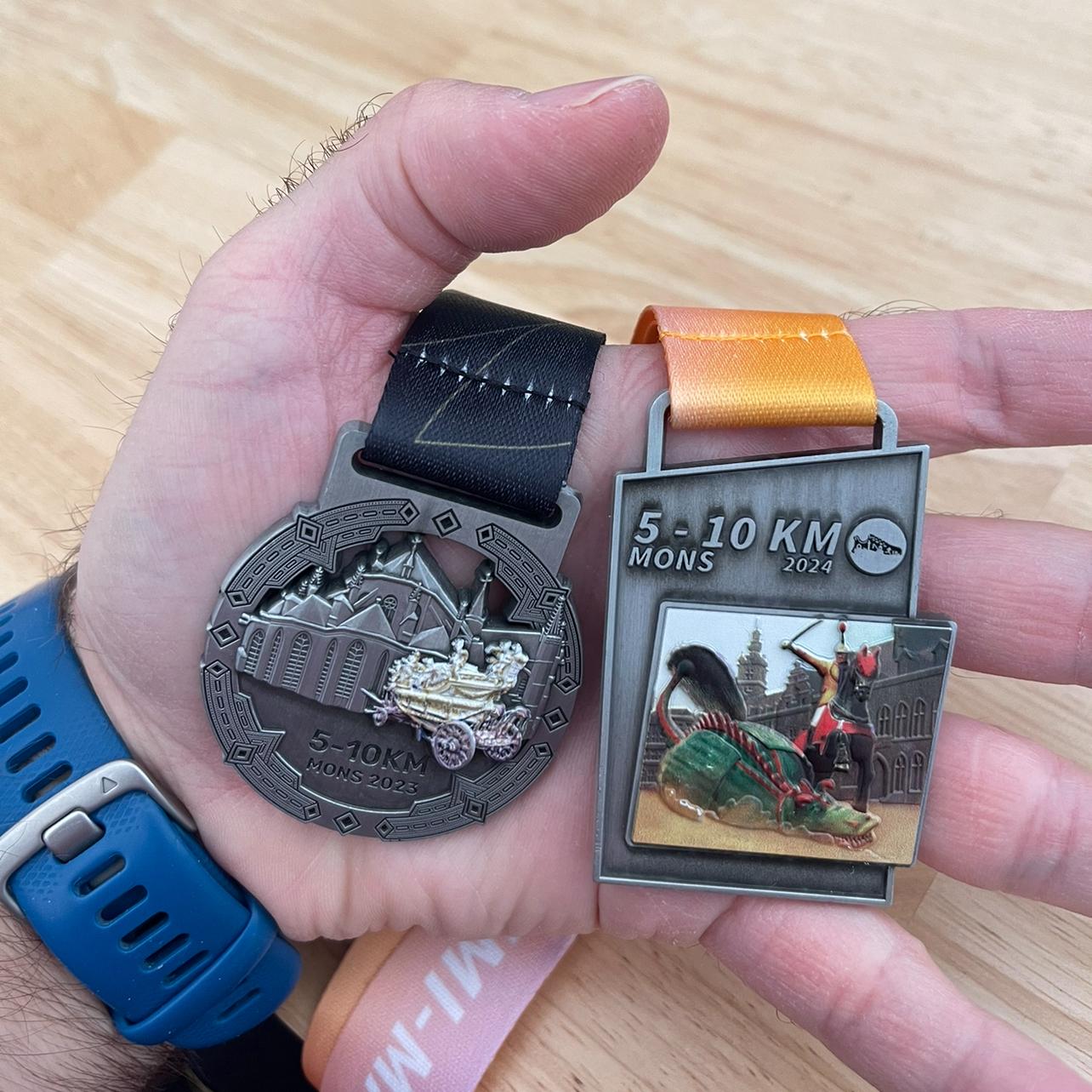 Runner holding two medals from Semi-Marathon de Mons 5K races, comparing 2023 and 2024 editions